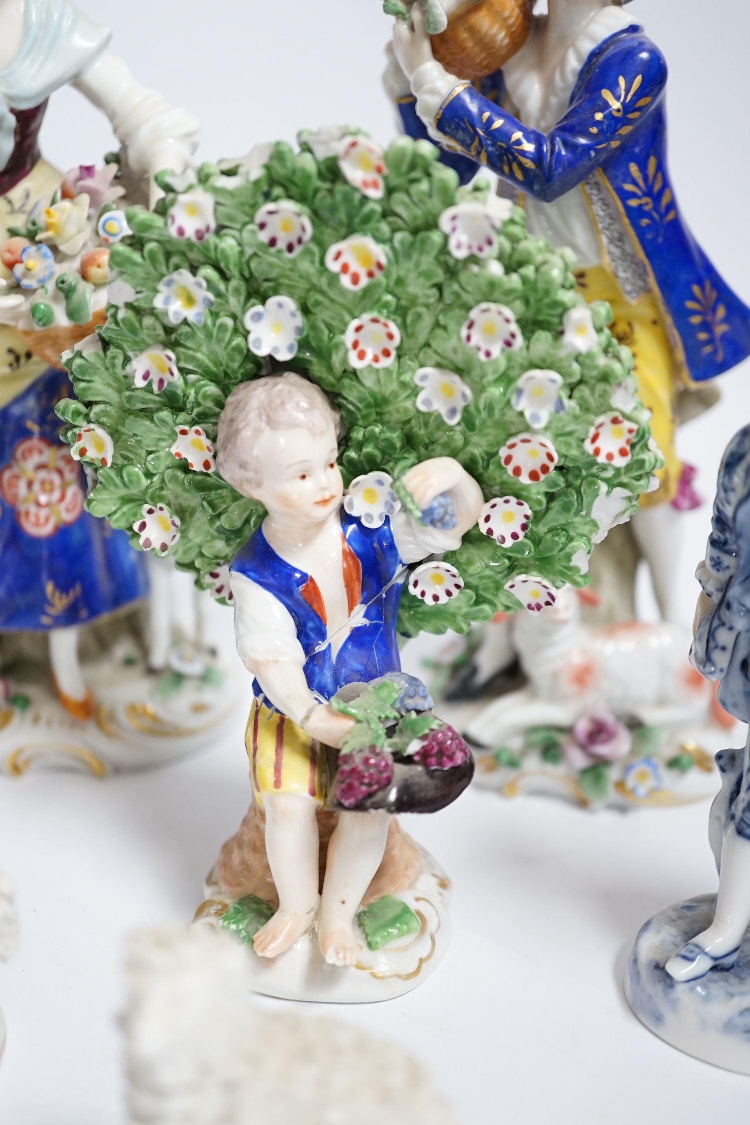 A pair of Derby style porcelain small bocage figures, a boy and girl seated with grape filled hats, height 14cm, three porcelain lambs and another figure